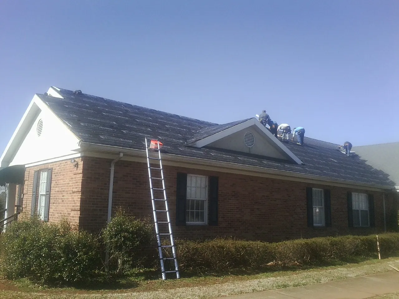 Crew tearing shingles off a brick ranch roof with a ladder set — Emergency Roof Repair work by our crew in Port Gamble