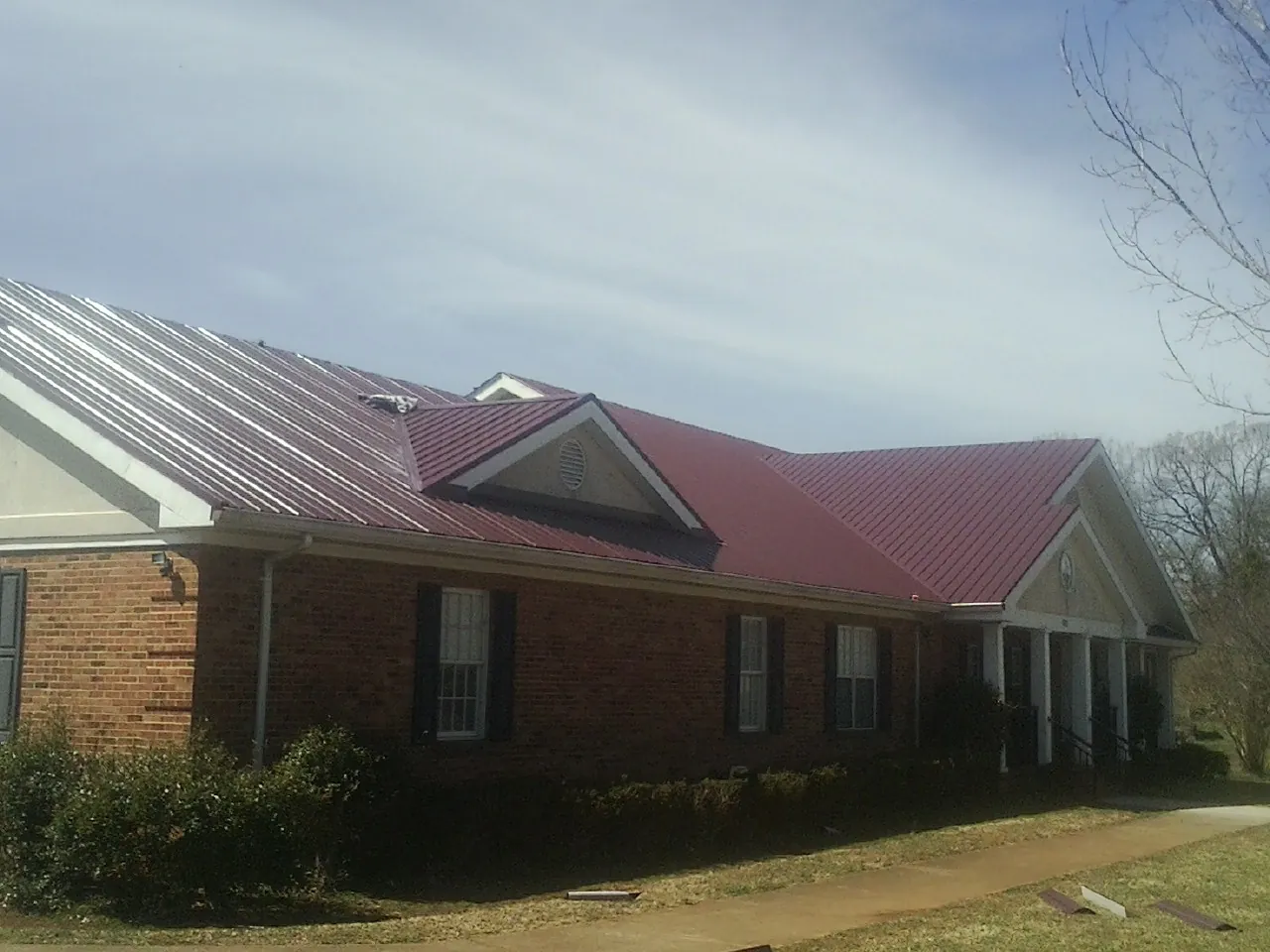 Red metal roof with gabled entries on a long brick building, from a Hail Damage Roof Repair job in Port Gamble