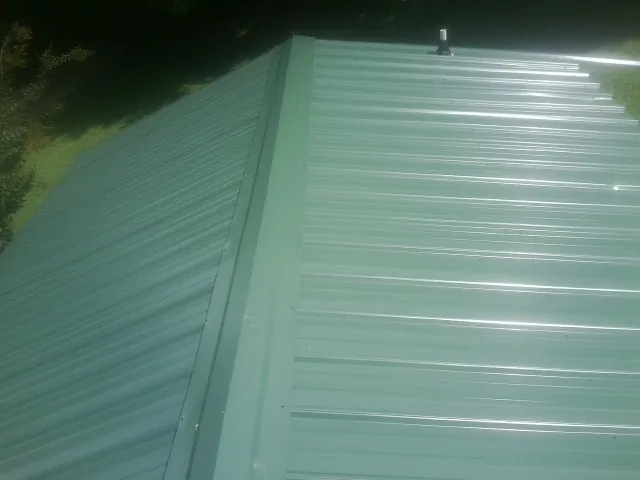 New green metal panels meeting at the ridge of a roof — Flat Roof Repair work by our crew in Port Gamble