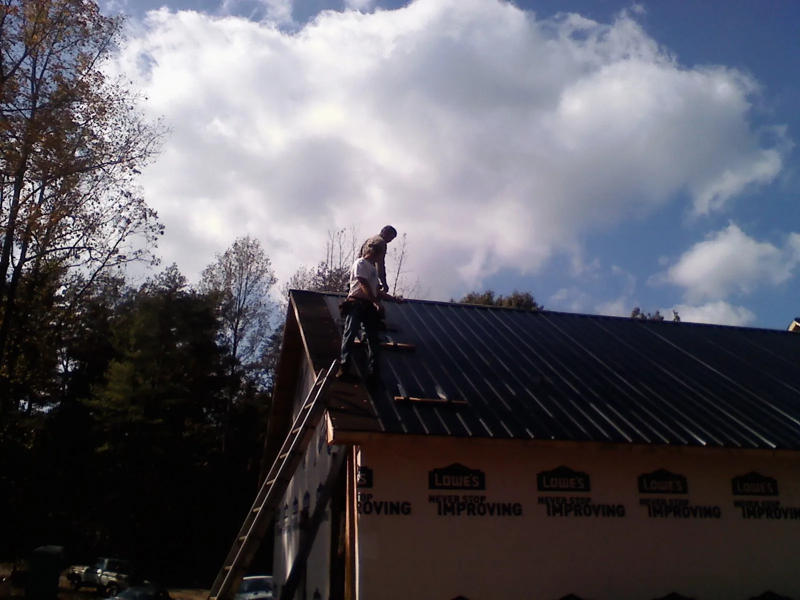 Roofer fastening dark metal panels high against a cloudy sky, from a Roof Inspection job in Port Gamble