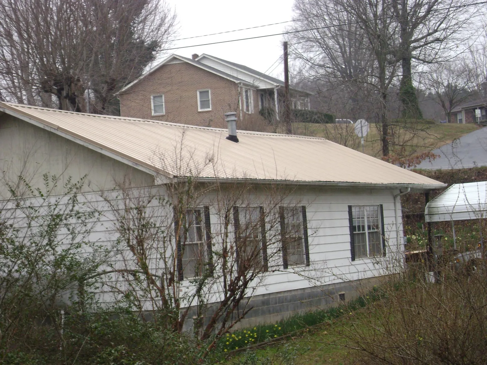 Tan metal roof on a white sided house set into a hillside — Commercial Roofing by Roofing Brothers in Port Gamble